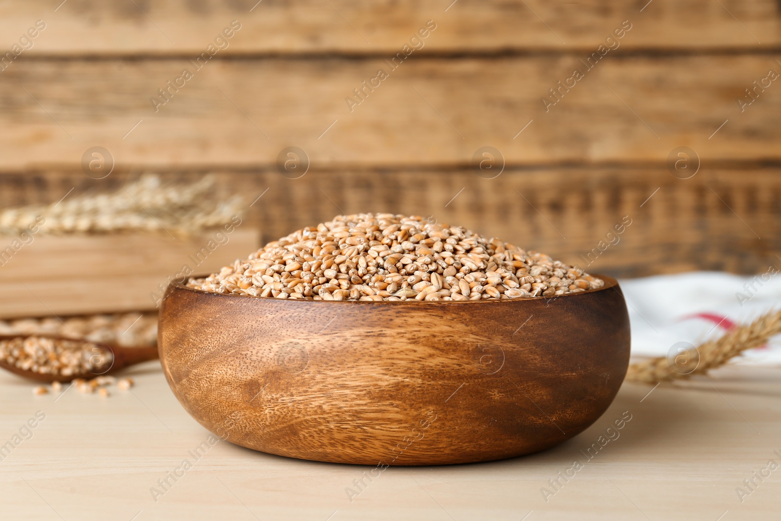 Photo of Bowl of wheat grains on white wooden table, closeup