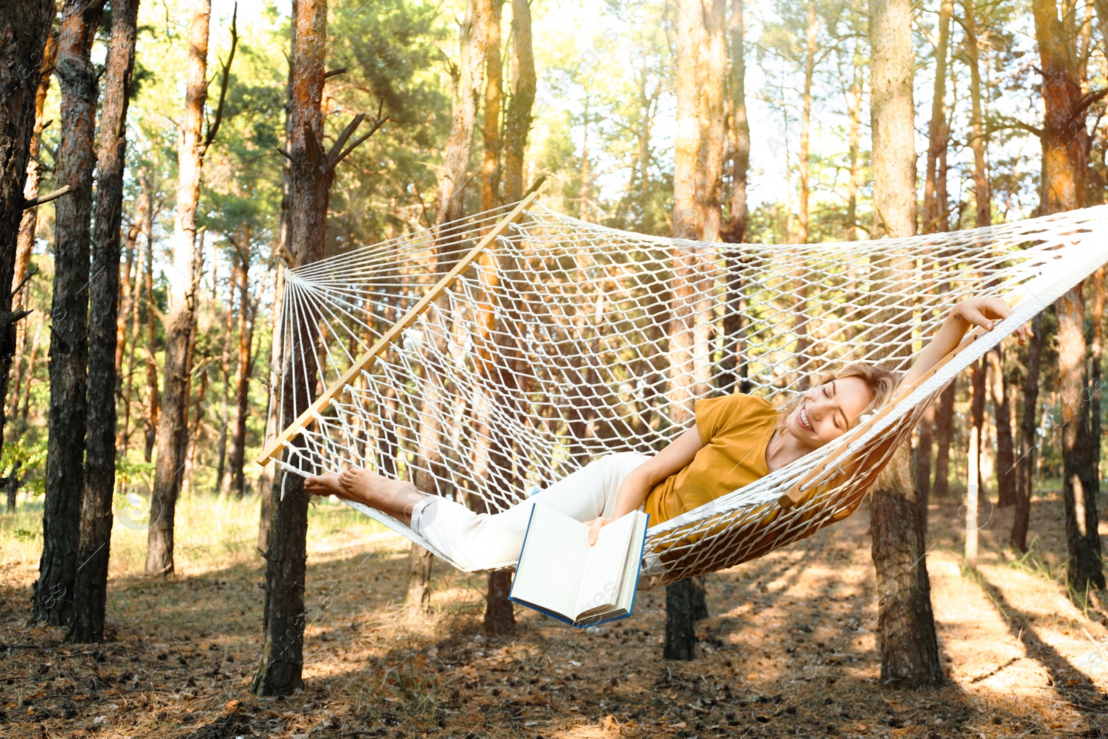 Photo of Happy young woman with book relaxing in hammock outdoors on summer day