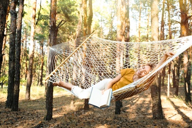 Photo of Happy young woman with book relaxing in hammock outdoors on summer day