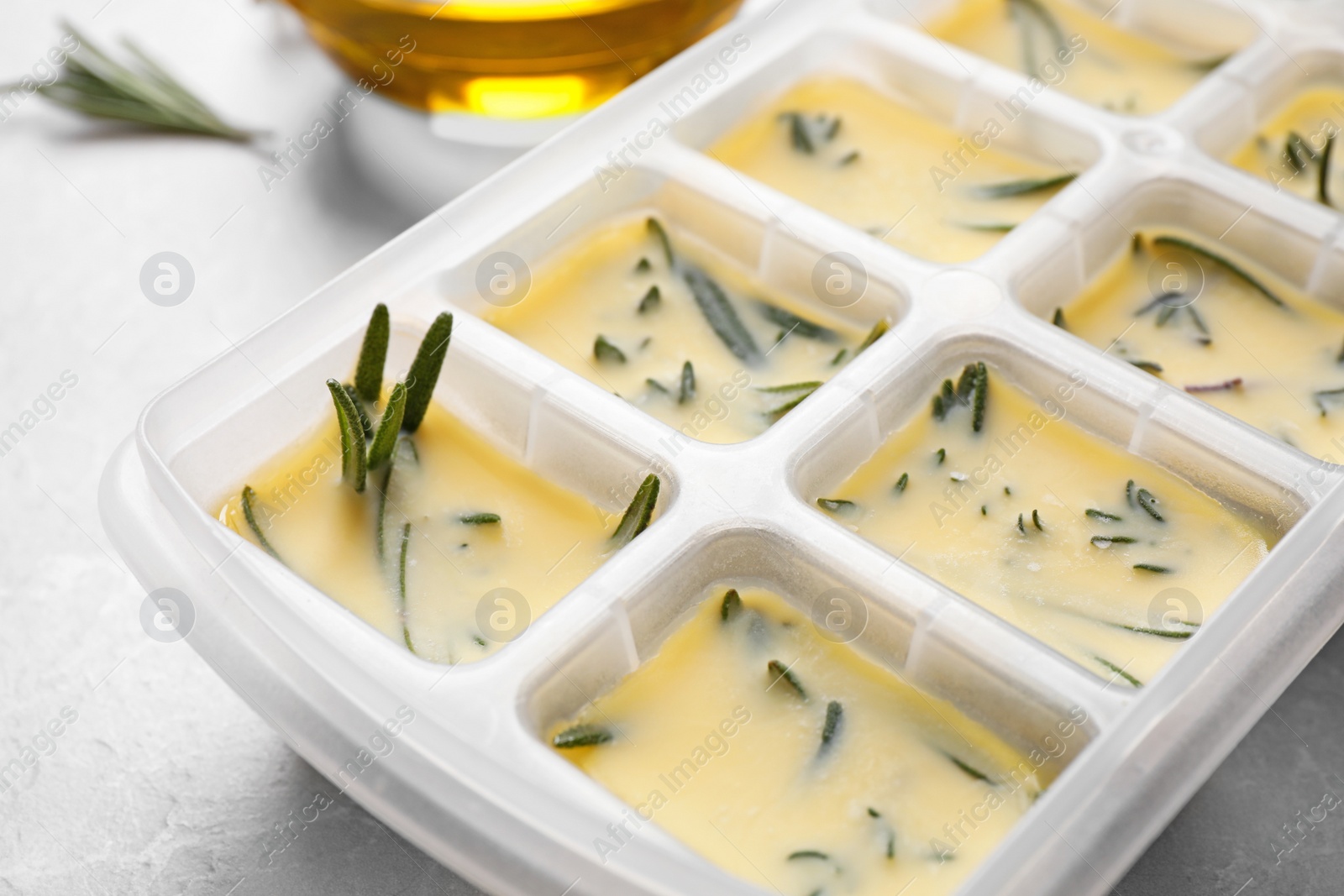 Photo of Ice cube tray with herbs frozen in oil and fresh rosemary on grey table, closeup