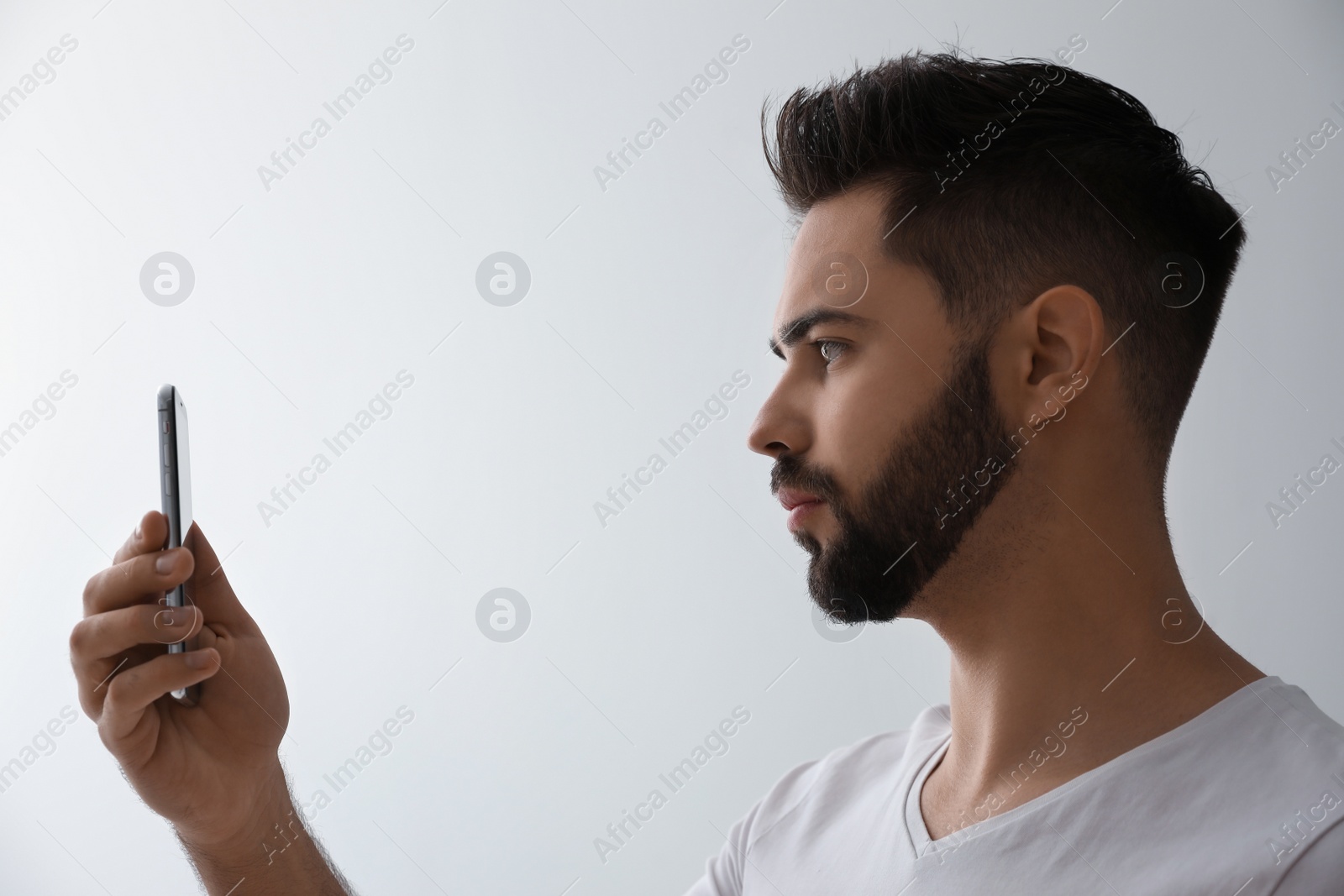 Photo of Young man unlocking smartphone with facial scanner on grey background. Biometric verification