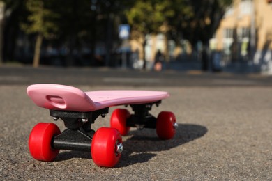 Pink skateboard with red wheels on asphalt outdoors