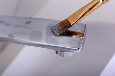 Using brush and powder to reveal fingerprints on faucet indoors, closeup