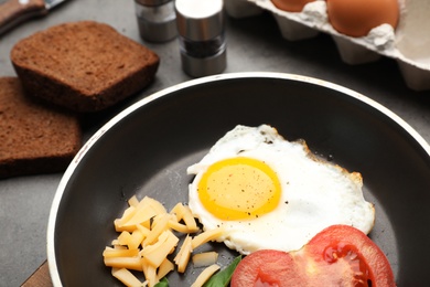 Pan with fried sunny side up egg, cheese and tomato on table, closeup