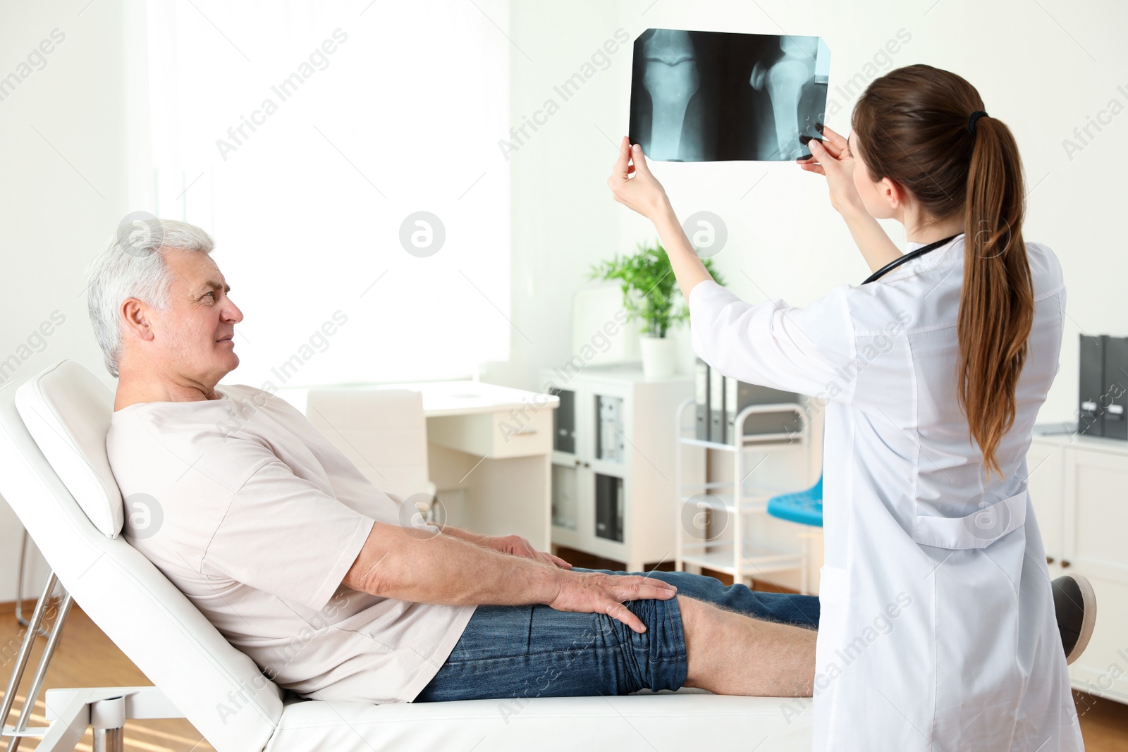 Photo of Young doctor with X-ray and senior patient in clinic. Knee problem