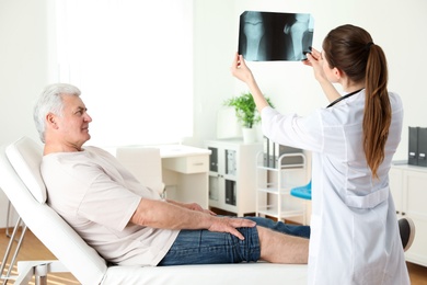 Photo of Young doctor with X-ray and senior patient in clinic. Knee problem