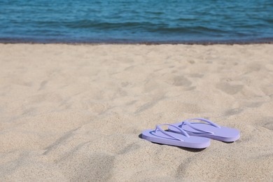 Photo of Stylish violet flip flops on beach sand, space for text