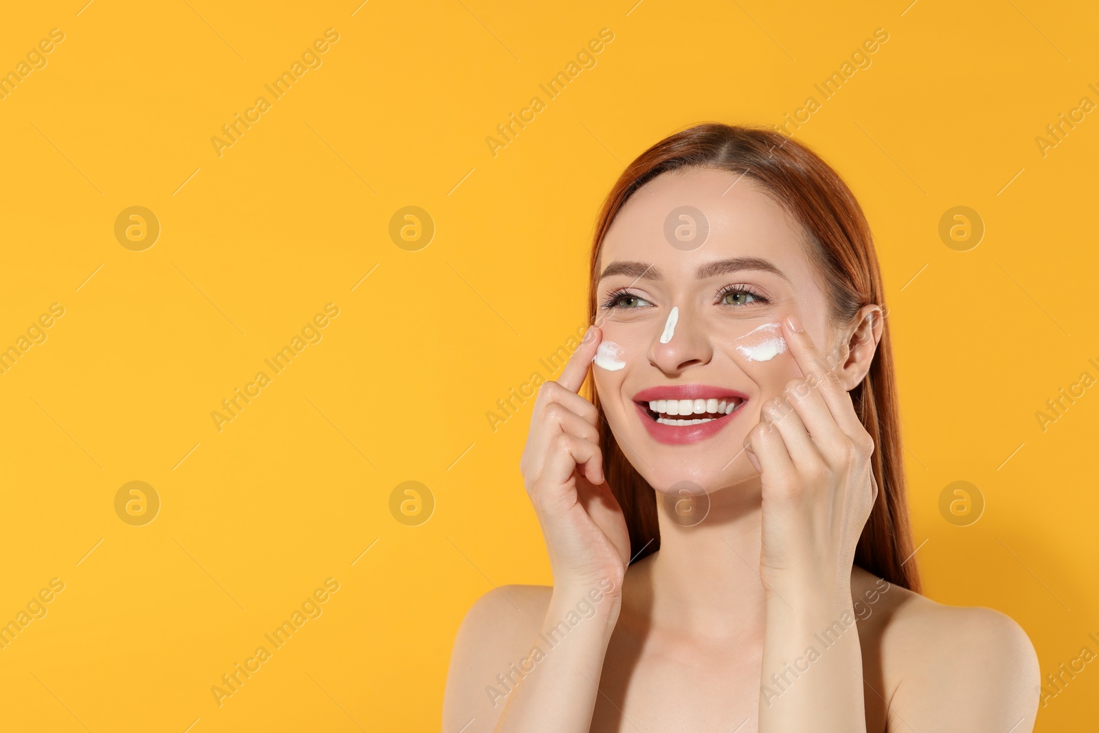 Photo of Beautiful young woman with sun protection cream on her face against orange background, space for text