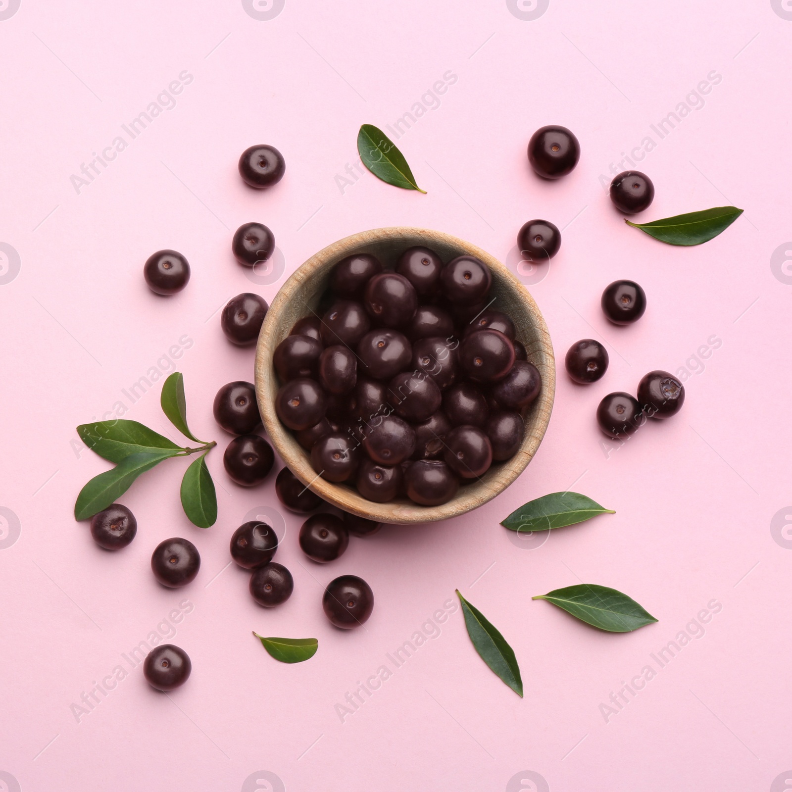 Photo of Acai berries and wooden bowl on pink background, flat lay