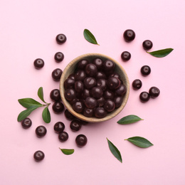 Photo of Acai berries and wooden bowl on pink background, flat lay