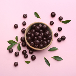 Acai berries and wooden bowl on pink background, flat lay