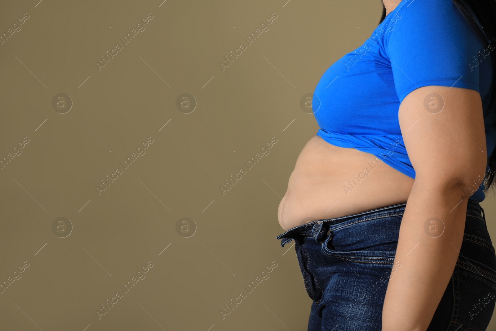 Photo of Overweight woman in tight shirt and jeans on light brown background, closeup. Space for text