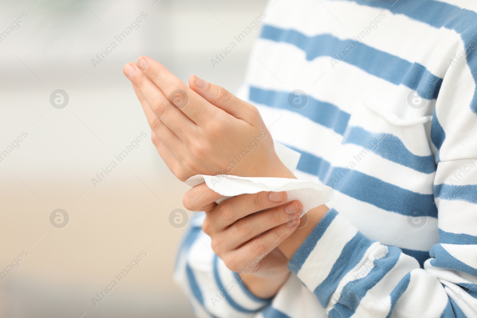 Photo of Woman cleaning hands with paper tissue on blurred background, closeup