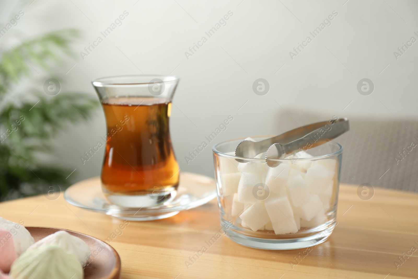 Photo of Woman adding sugar cube into aromatic tea at wooden table indoors, closeup