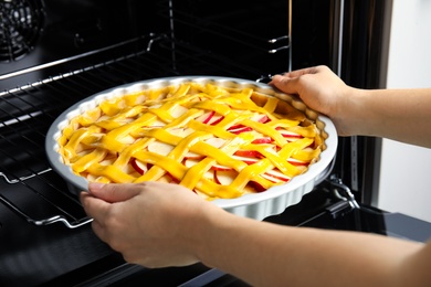 Photo of Woman putting raw traditional English apple pie into oven, closeup