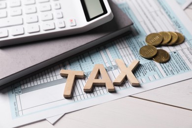 Photo of Word Tax made with letters, calculator, document, notebook and coins on white wooden table, closeup