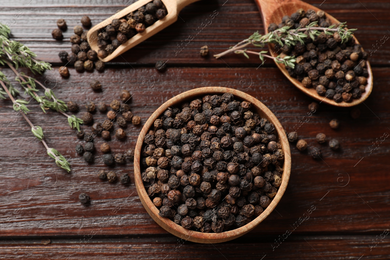 Photo of Aromatic spice. Black pepper in bowl, spoon and scoop on wooden table, flat lay