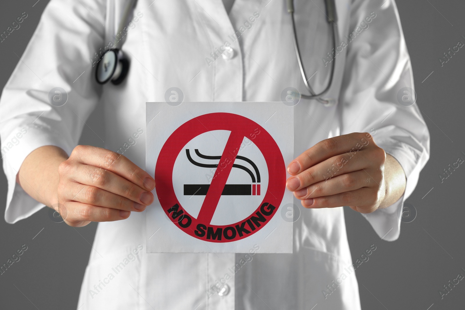 Photo of Doctor holding card with no smoking sign on gray background, closeup