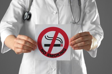 Photo of Doctor holding card with no smoking sign on gray background, closeup