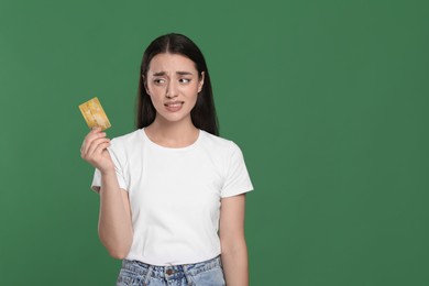 Confused woman with credit card on green background, space for text. Debt problem