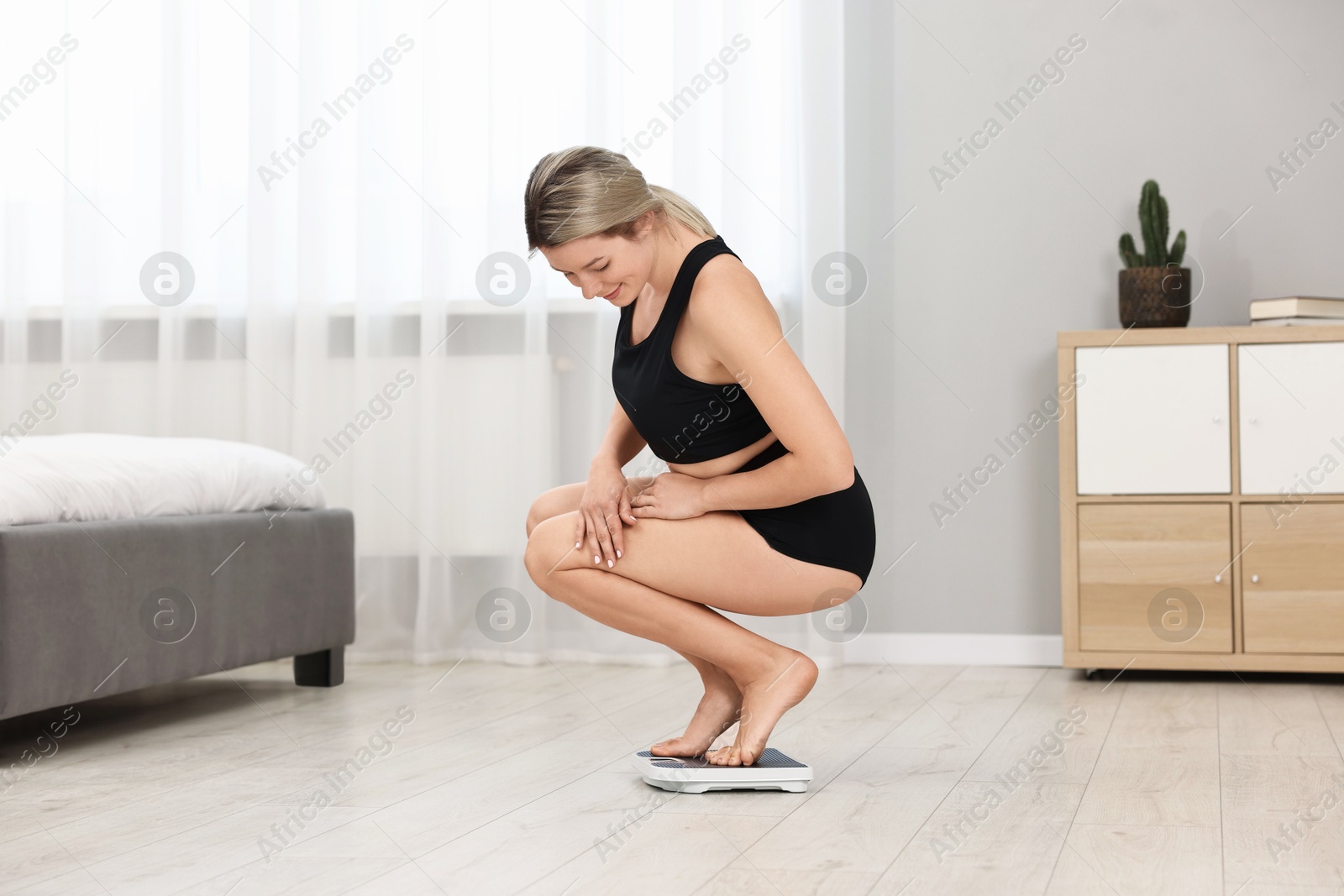 Photo of Happy woman standing on floor scales at home