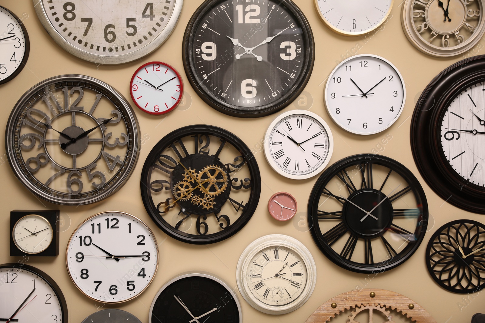 Photo of Collection of stylish clocks on beige wall