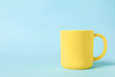 Photo of One yellow ceramic mug on light blue background, space for text