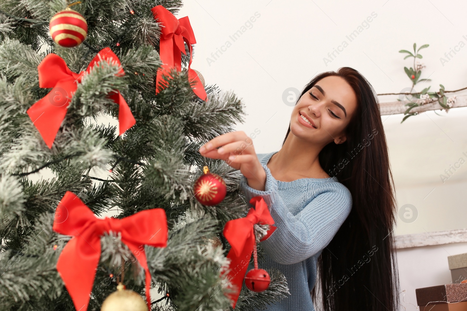 Photo of Beautiful young woman decorating Christmas tree at home