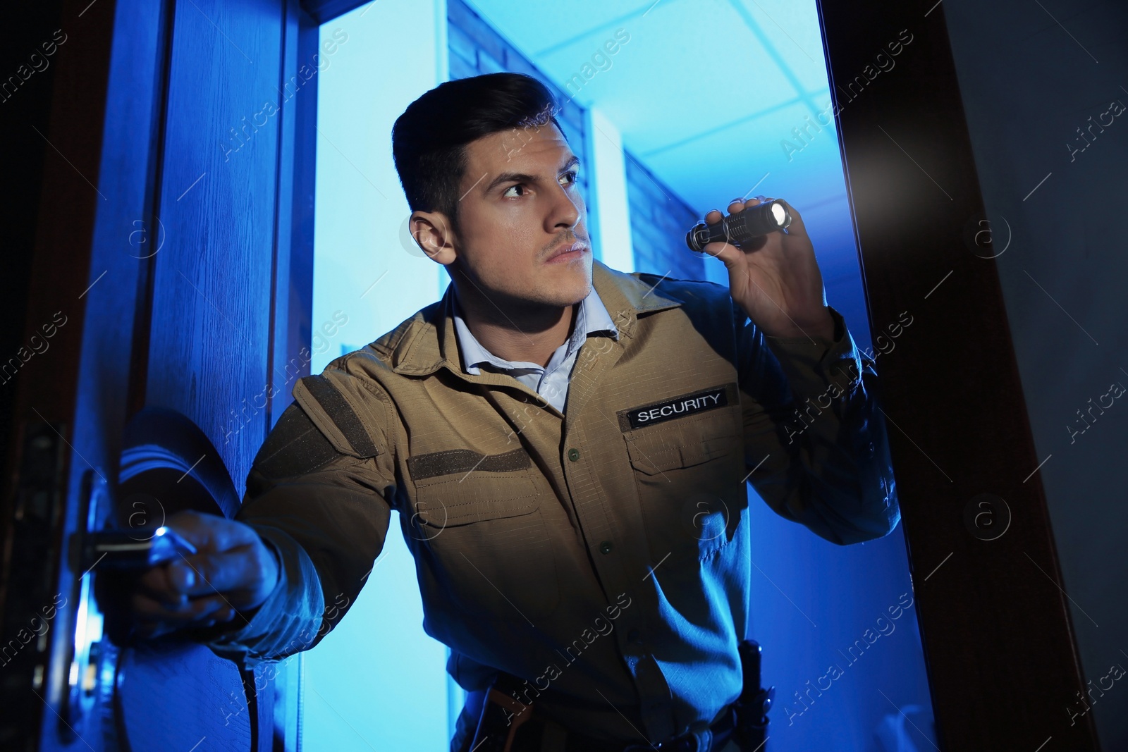 Photo of Professional security guard with flashlight checking dark room