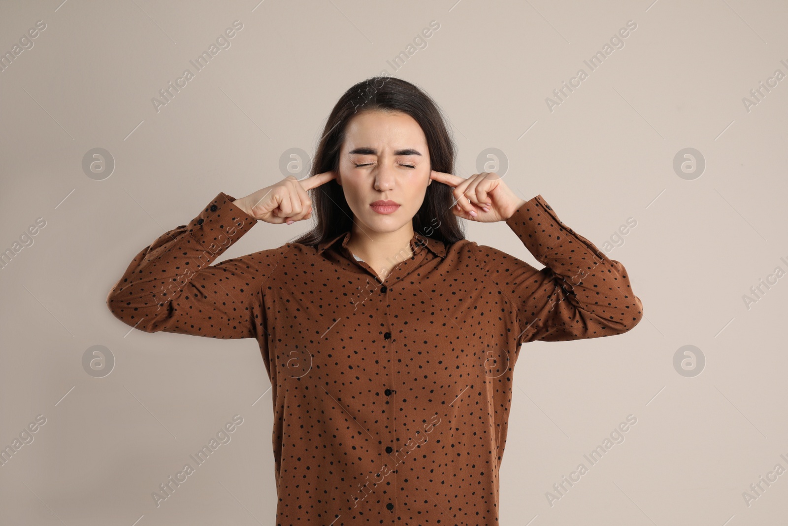 Photo of Young woman covering ears with fingers on beige background