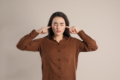 Young woman covering ears with fingers on beige background