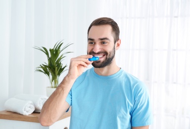 Photo of Young man using teeth whitening device at home