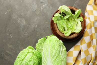 Photo of Fresh ripe Chinese cabbages and green leaves in bowl on gray textured table, flat lay. Space for text