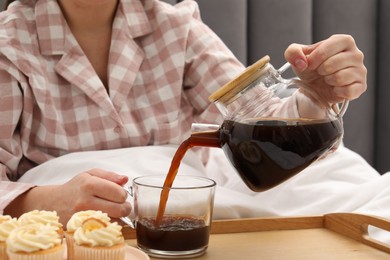 Photo of Woman pouring hot drink into cup in bed, closeup