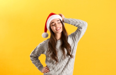 Beautiful woman wearing Santa Claus hat on yellow background