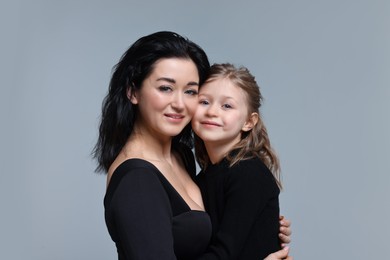 Beautiful mother hugging with little daughter on grey background