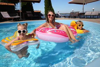 Young woman and her children with inflatable rings  in outdoor swimming pool on sunny summer day