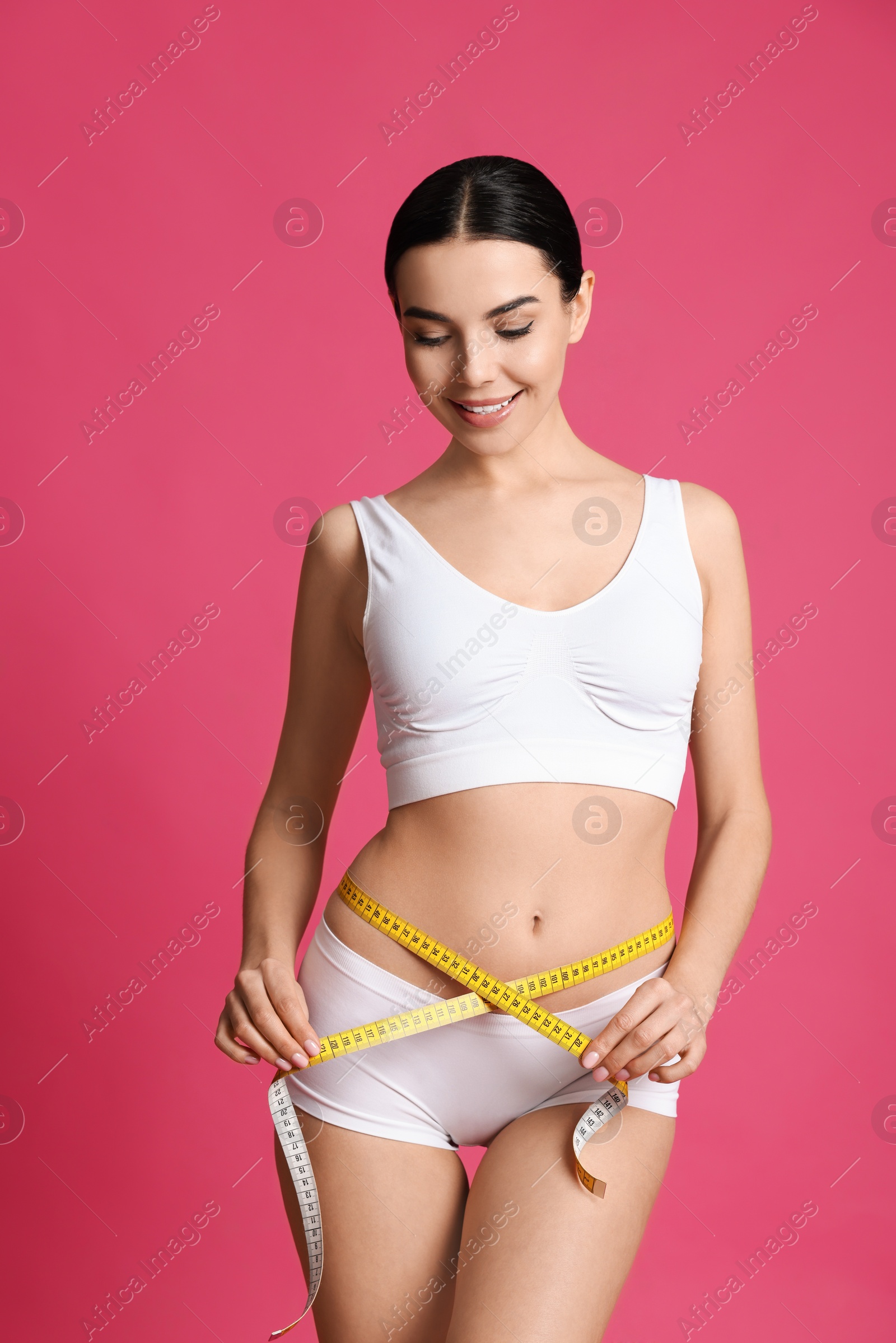 Photo of Young woman measuring waist with tape on pink background