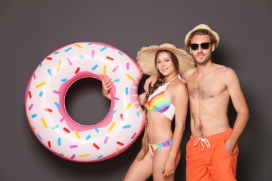 Young couple in beachwear with inflatable ring on dark background