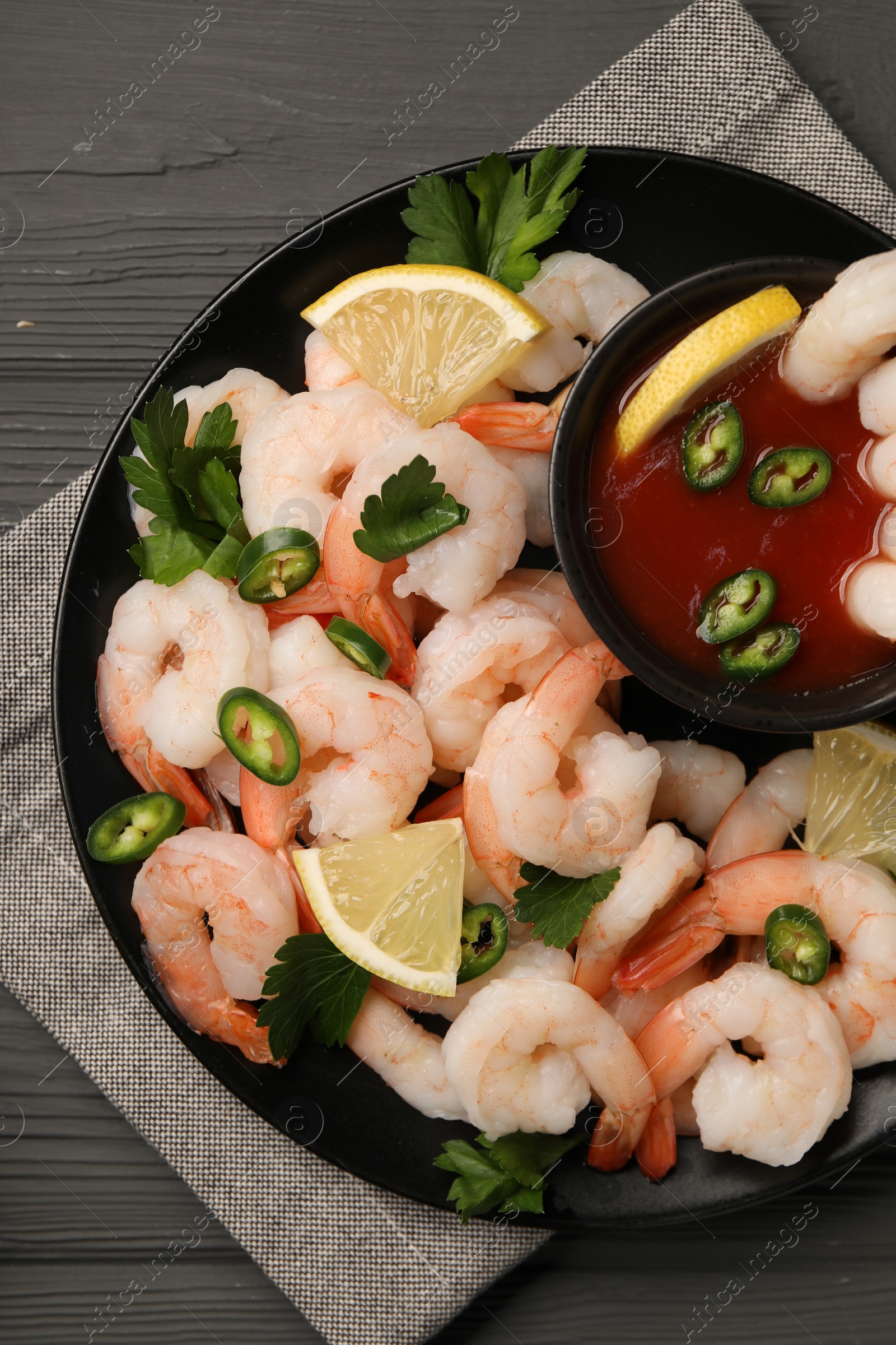 Photo of Tasty boiled shrimps with cocktail sauce, chili, parsley and lemon on grey wooden table, top view