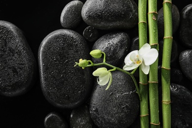 Photo of Bamboo branches with spa stones and orchid on black background, top view