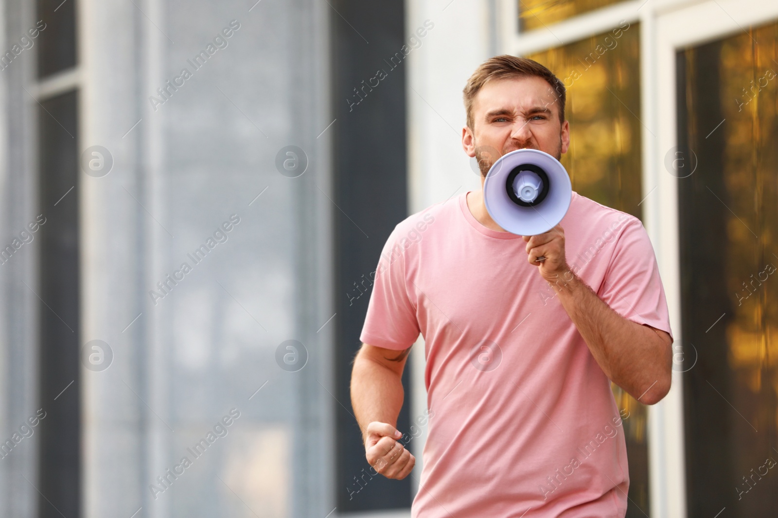 Image of Emotional young man with megaphone outdoors. Protest leader