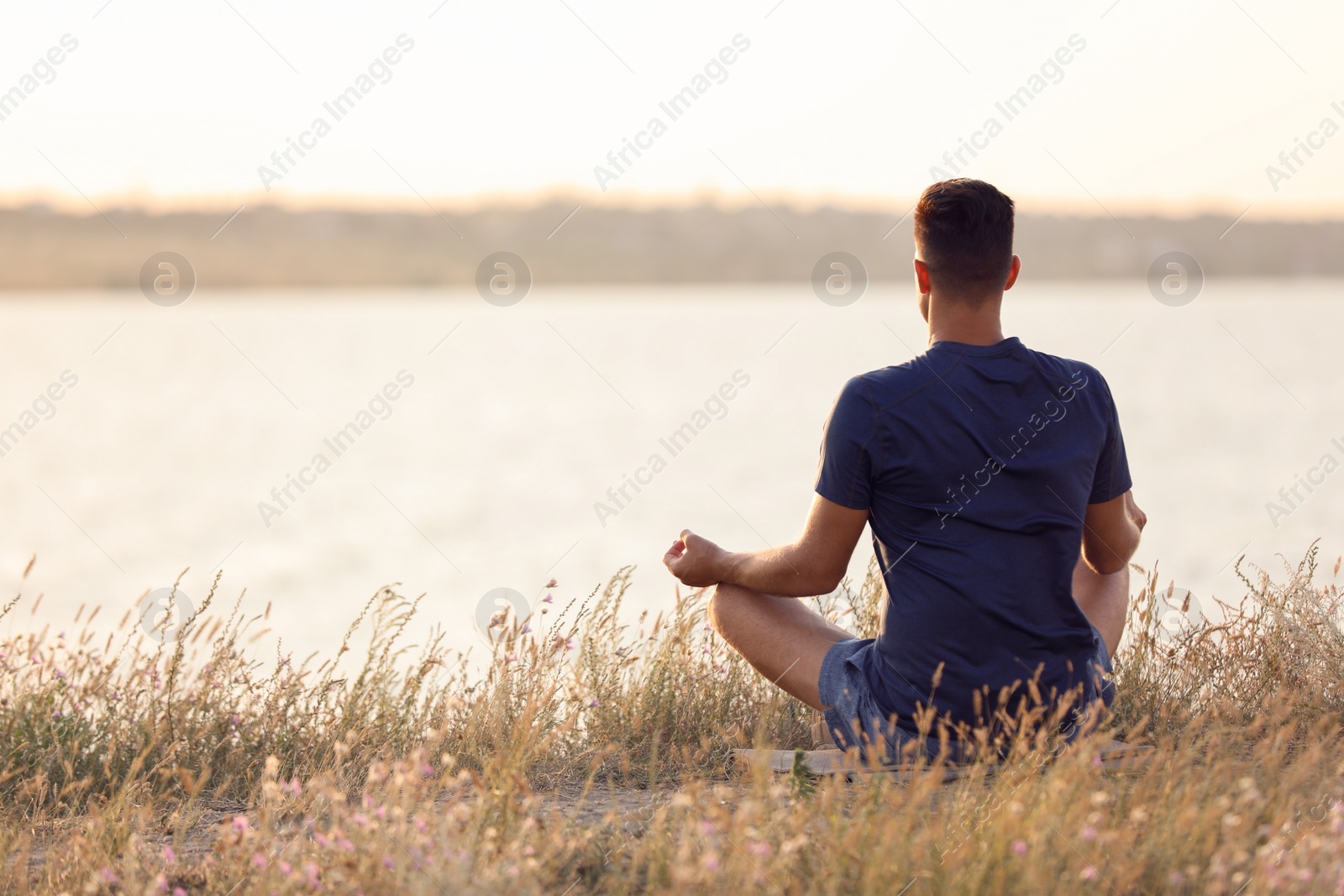 Photo of Man meditating near river on sunny day, back view. Space for text