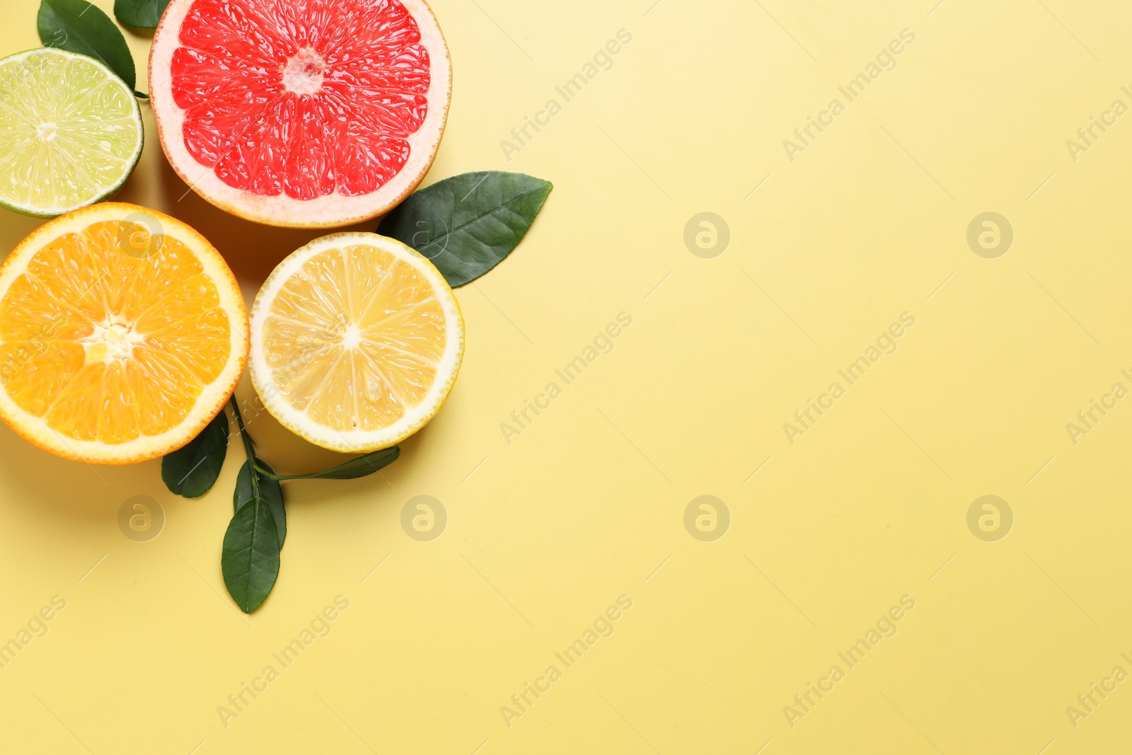 Photo of Different cut citrus fruits and leaves on yellow table, flat lay. Space for text