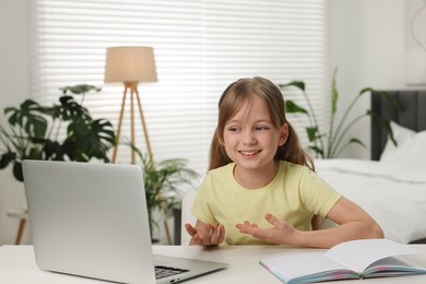 Cute girl having video chat via laptop at table indoors