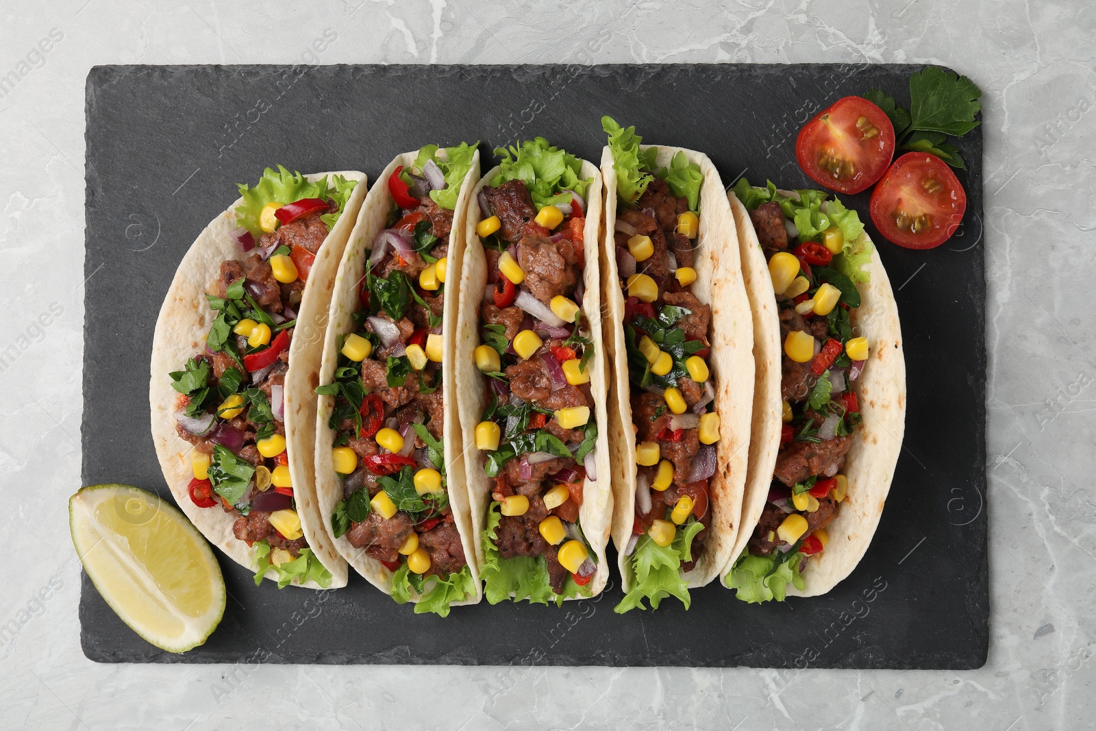 Photo of Delicious tacos with meat, vegetables and lime on light gray marble table, top view