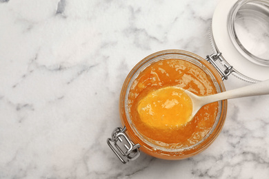 Photo of Homemade delicious orange jam on marble table, top view. Space for text