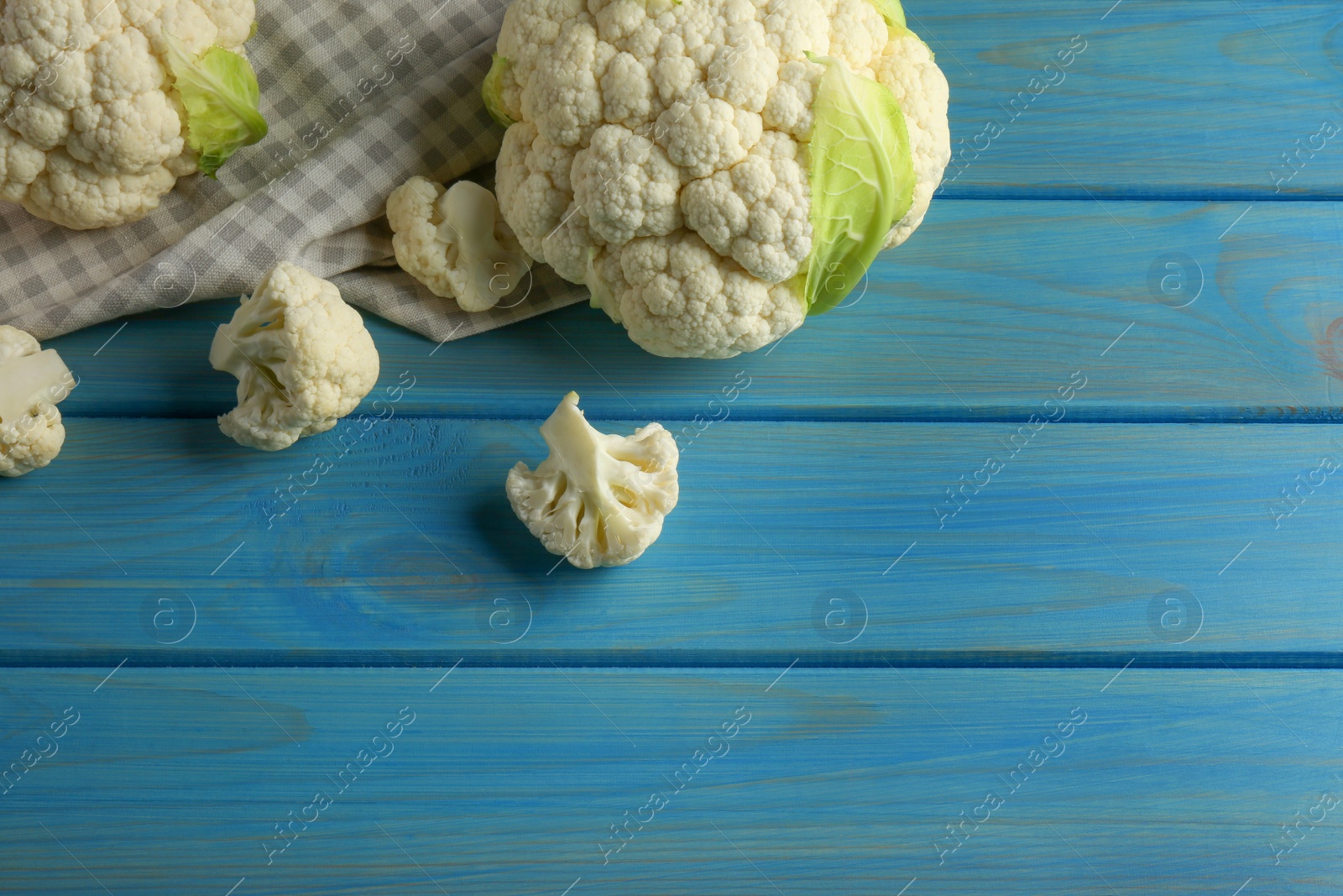 Photo of Fresh whole and cut cauliflowers on light blue wooden table. Space for text