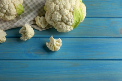 Fresh whole and cut cauliflowers on light blue wooden table. Space for text