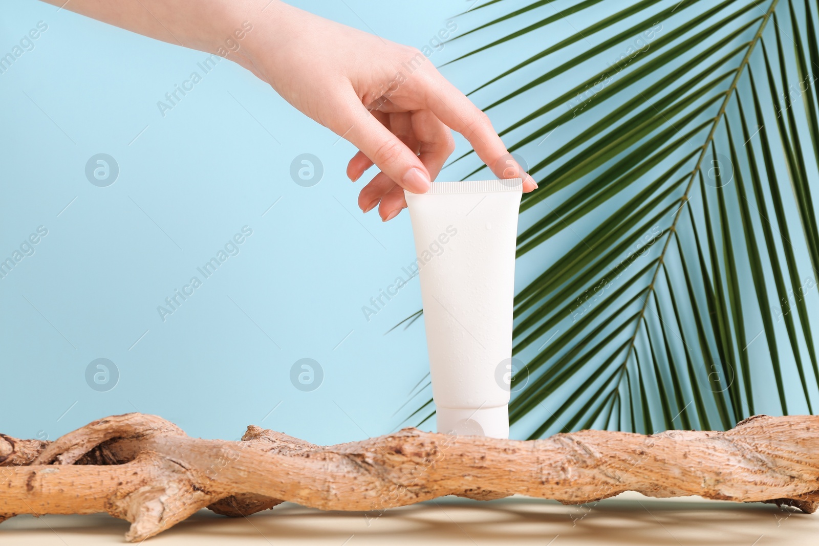 Photo of Woman with tube of cream and plant against light blue background, closeup